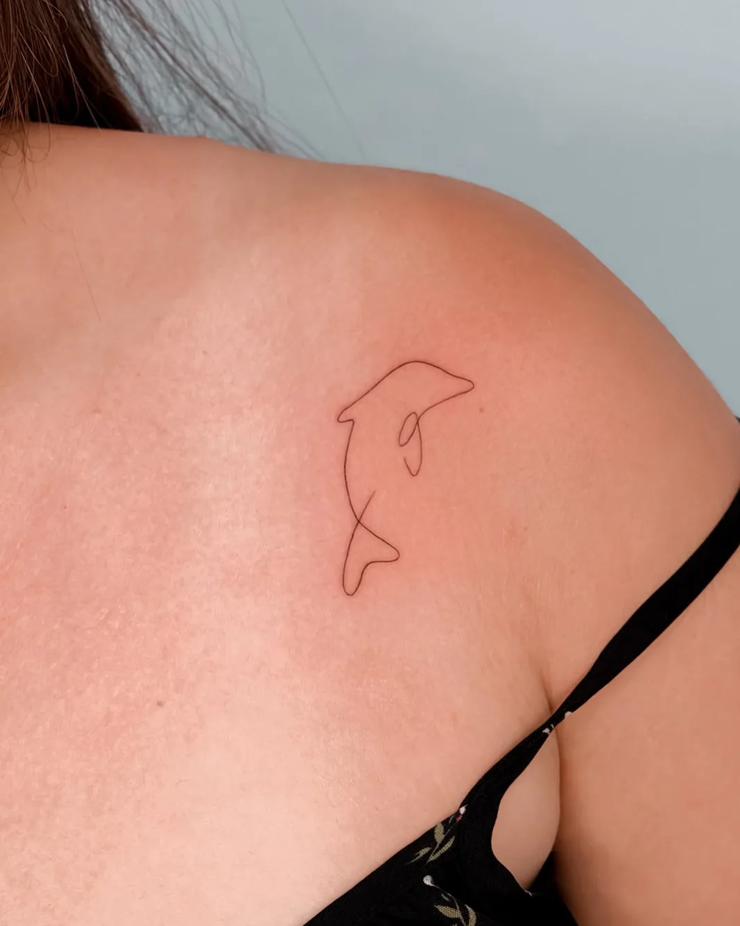Fine line single line dolphin tattoo on the collarbone