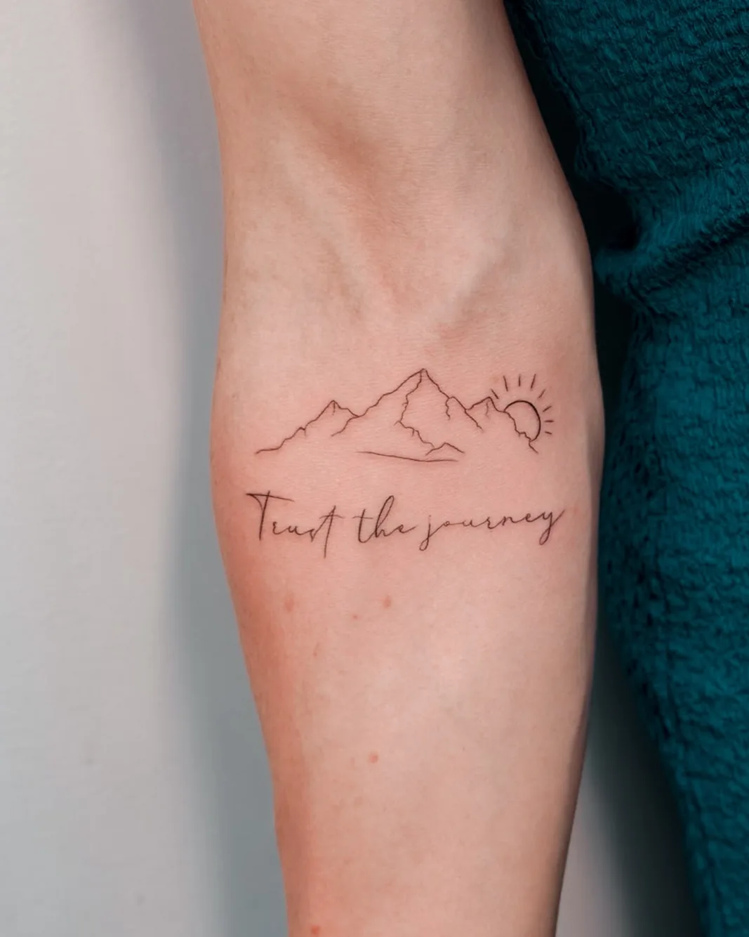 Fine line mountains, sun and lettering tattoo on the forearm