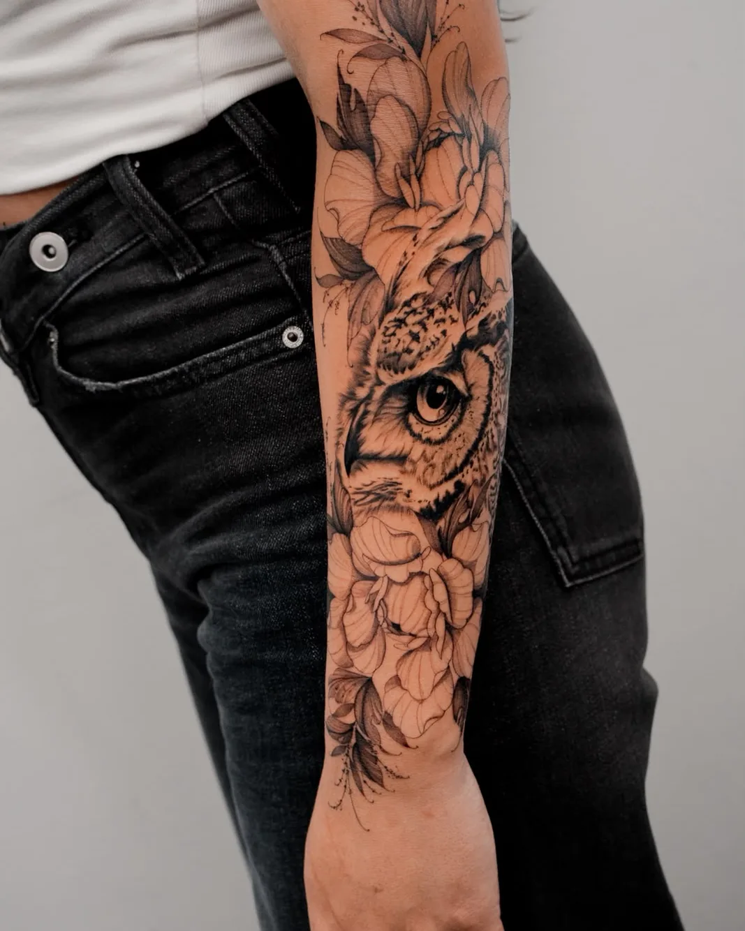 Botanical owl portrait framed by fine line flowers tattoo on the forearm