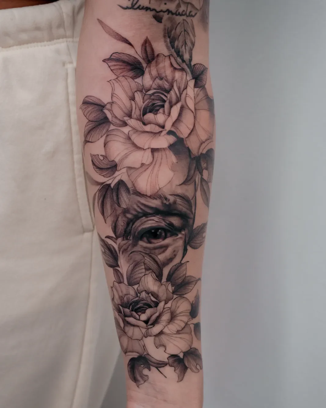 Botanical roses and hidden eye tattoo on the forearm