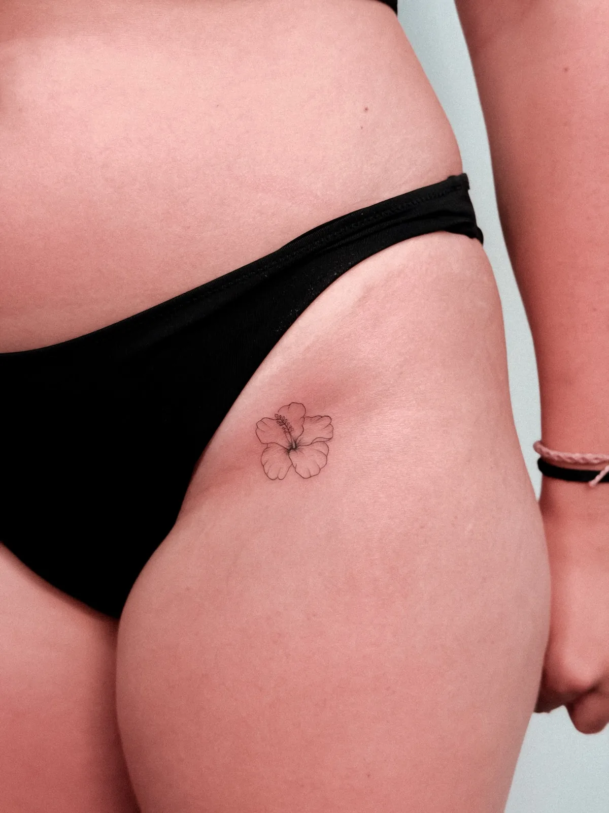 Fine line hibiscus on the hip — tattoo by Hugo Gonzalez, Funchal, Madeira