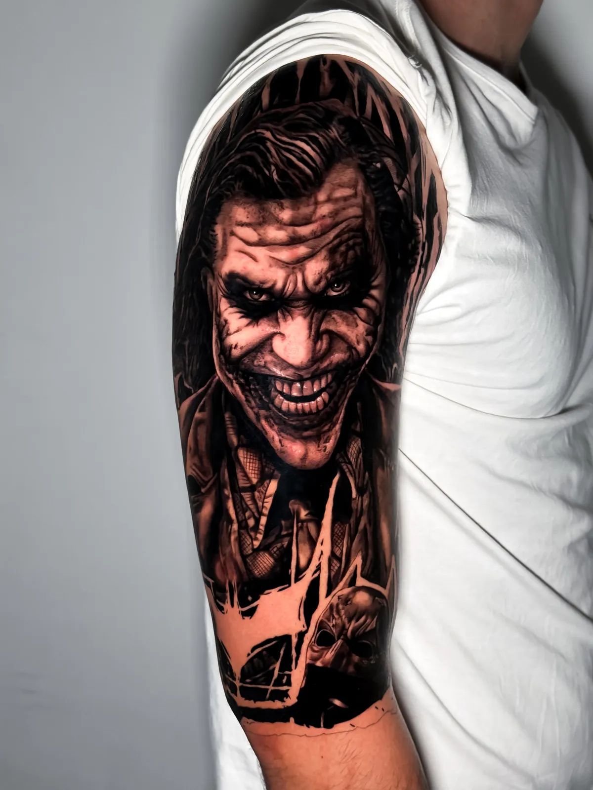 Black and grey Joker portrait on the upper arm by Hugo Gonzalez